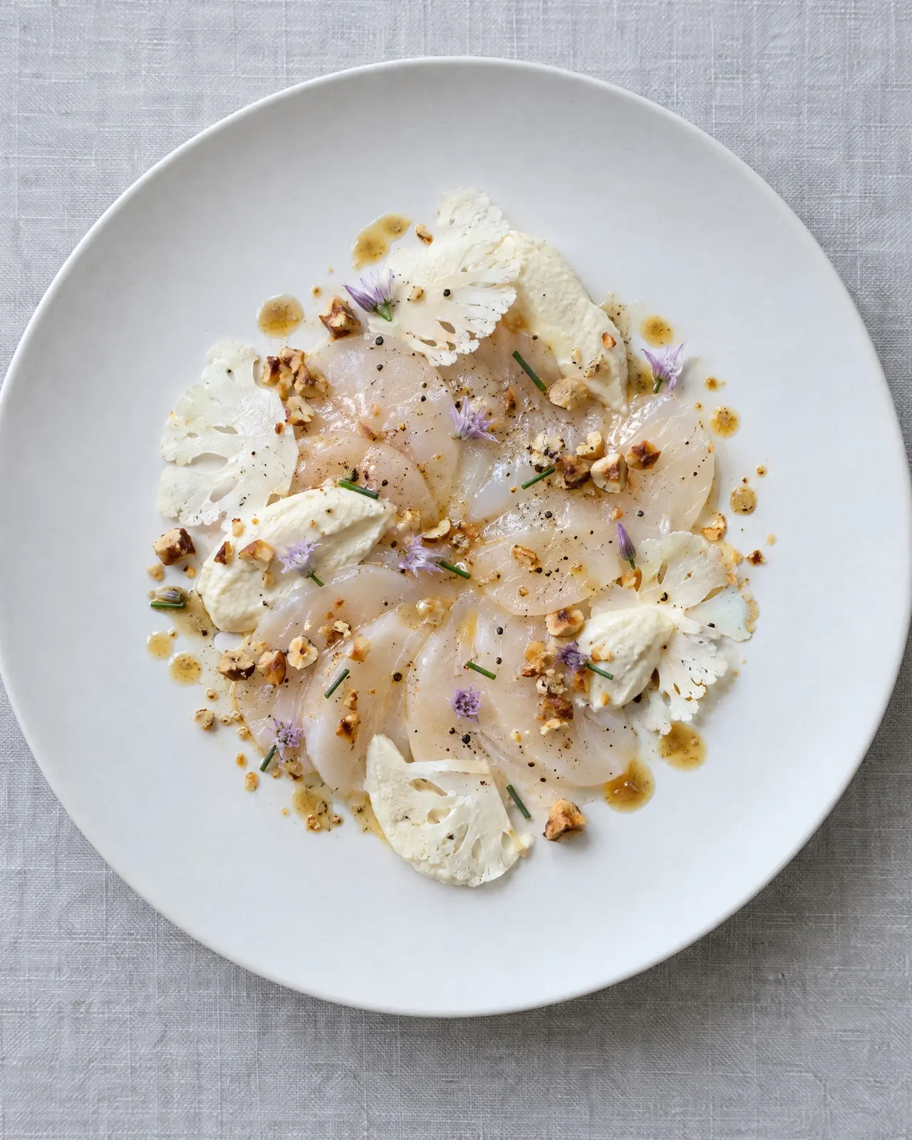 Saint-Jacques crues en pétales, chou-fleur cru et en purée, noisettes torréfiées et fleurs de ciboulette, vues du dessus